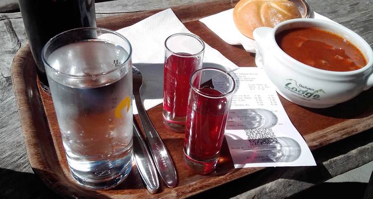 Plateau avec verre d'eau, verres de schnaps rouge, bol de soupe et reçu sur une table en bois rustique