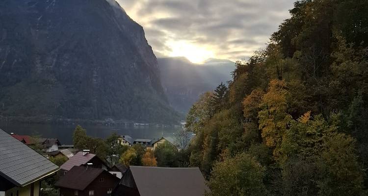 Village de montagne au bord du lac avec les premiers rayons du soleil perçant les nuages au-dessus de falaises abruptes
