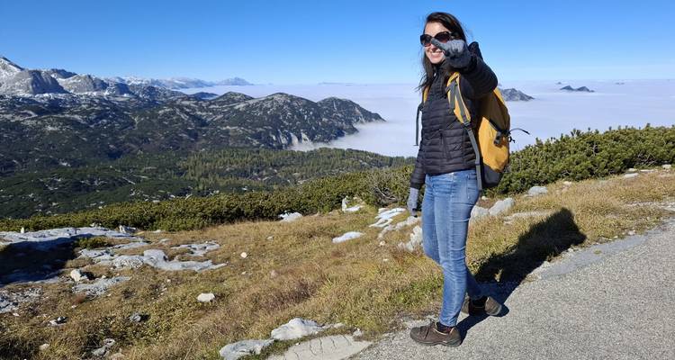 Randonneur souriant pointant du doigt vers l'appareil photo sur un sentier de montagne au-dessus d'une inversion de nuages