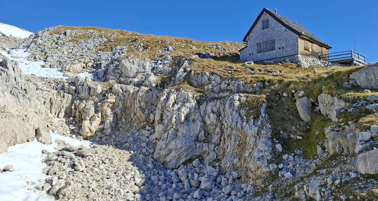 Petit refuge alpin perché sur une pente rocheuse entourée d'éboulis et de neige persistante