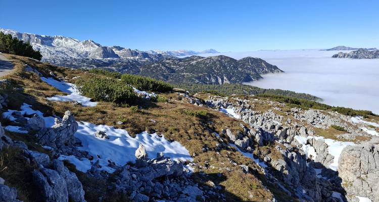 Terrain alpin rocheux avec des poches de neige dominant les crêtes lointaines et une mer de nuages