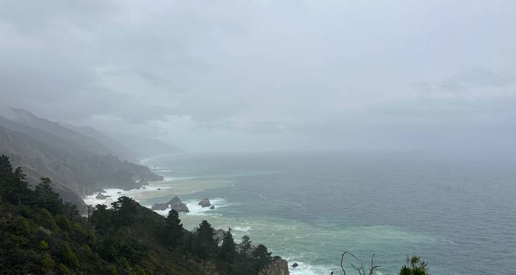 Misty coastal mountains fading into the distance over a grey, choppy sea.