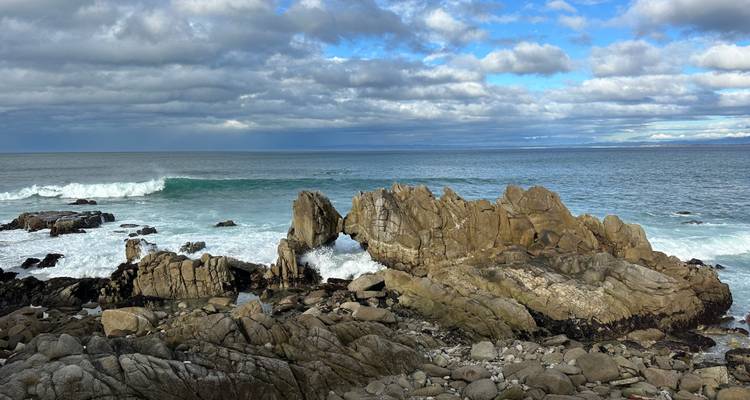 Rocky coastal arch formation battered by turquoise waves under a bright sky.