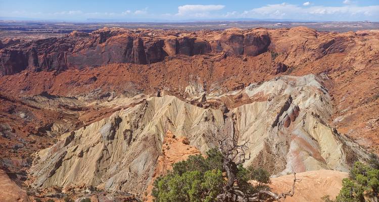 Colorful eroded cliffs revealing tilted multicolored strata amid a desert canyon basin.
