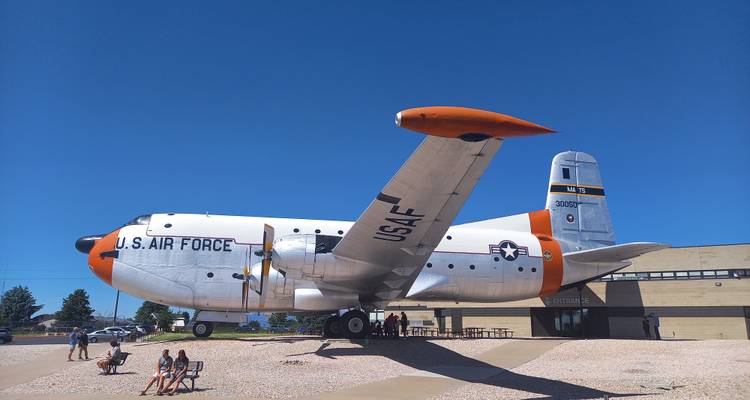 Large U.S. Air Force cargo plane displayed outdoors with visitors resting on benches below.