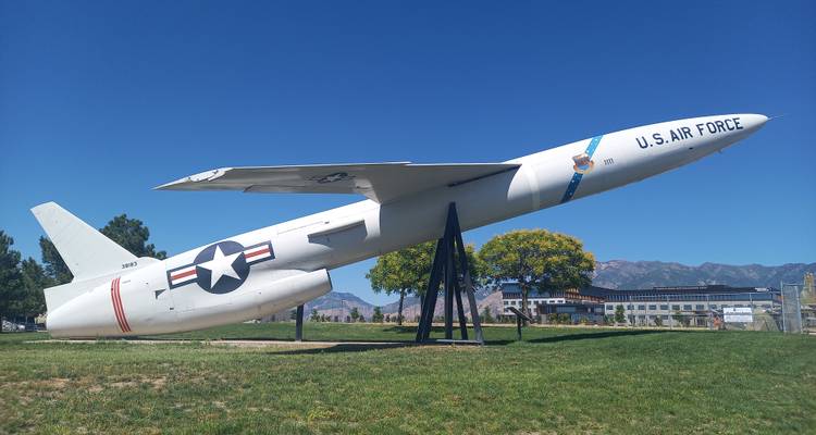 White U.S. Air Force missile-like jet mounted on supports against a blue sky and mountain backdrop.
