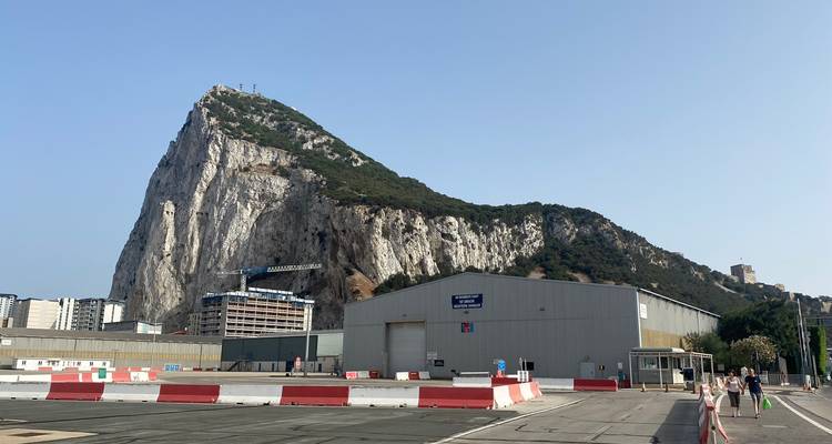 Impressive view of the Rock of Gibraltar rising steeply behind airport service buildings and barriers.