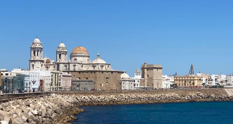 Seafront panorama of Cádiz with its golden-domed cathedral and historic towers above a protective stone seawall.