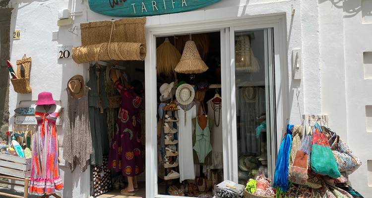 Charming boutique shop in Tarifa selling beachwear, hats and colorful textiles, with a customer browsing inside.