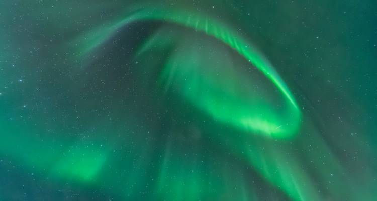 Spiraalvormige lus van helder groene aurora tegen een donkere sterrenhemel.