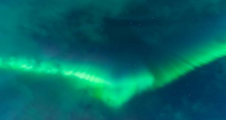 Horizontaal uitgerekte groene aurora gedeeltelijk verborgen door kolkende wolken.