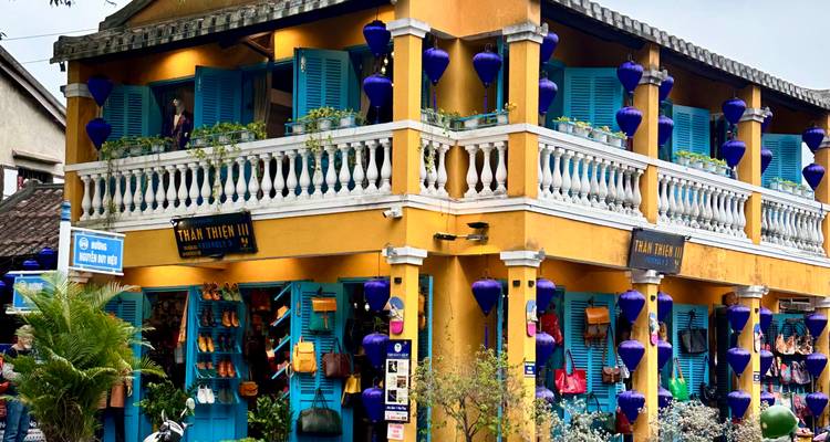 Lebendiges gelbes Shophouse mit türkisfarbenen Läden und hängenden blauen Laternen an einer Straßenecke in Hoi An.