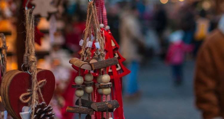 Close-up of handcrafted wooden and bead ornaments hanging at a bustling Christmas market stall.