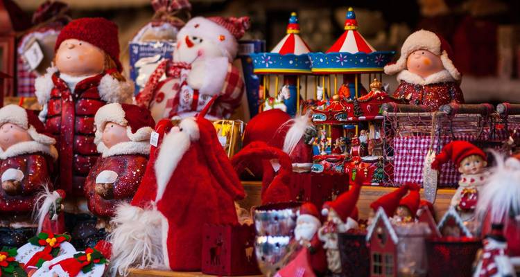 Colorful assortment of plush Santa figurines and toys on a Christmas market stall.