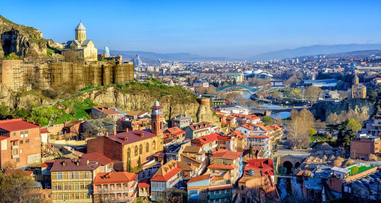 Vista diurna sobre los tejadillos coloridos de Tiflis, las murallas de la fortaleza y el valle del río.