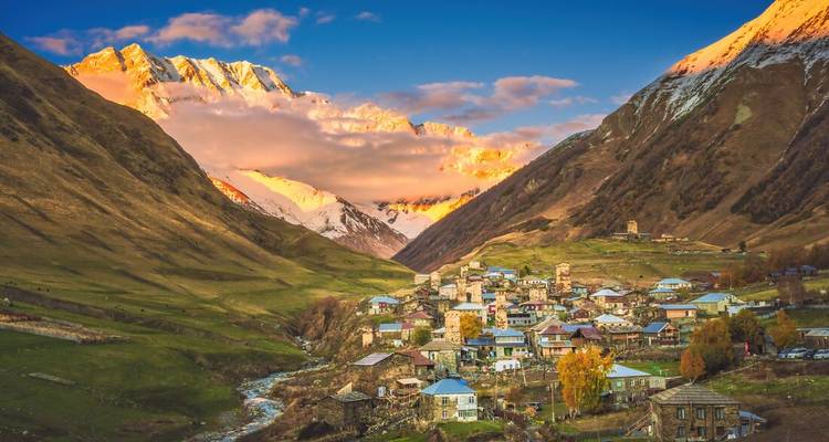 Alpine village of Ushguli nestled between steep valleys with snow-capped Caucasus peaks glowing in sunset light.