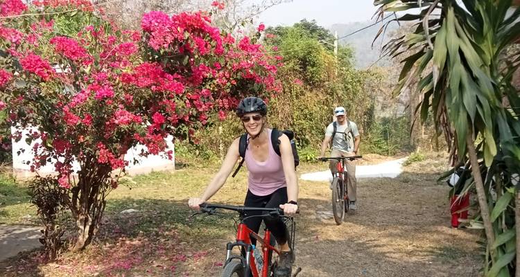 Smiling cyclists pass vibrant pink bougainvillea blossoms on a garden path.