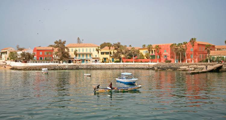 Colourful colonial houses lining the waterfront on Gorée Island with fishermen in a small boat.