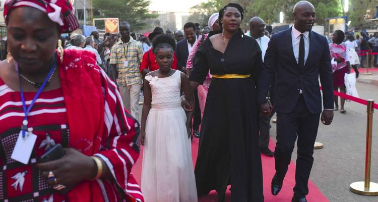 Crowds dressed for an outdoor red-carpet event with parents holding child's hands.