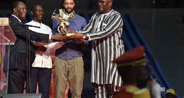 Group of men on stage jointly holding a trophy during formal awards presentation.