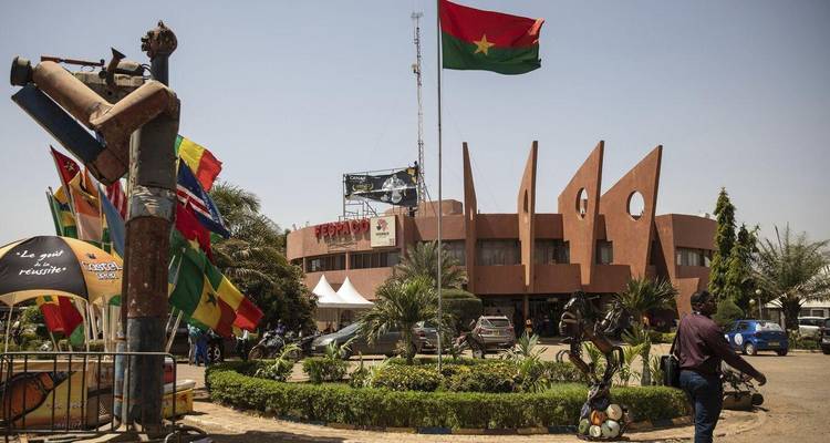 Modern circular building with Burkina Faso flag flying high and sculptures in landscaped roundabout.