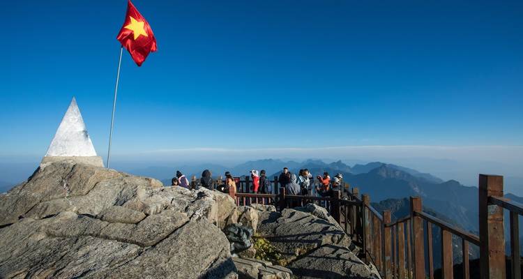 Besucher versammelten sich auf einer felsigen Gipfelplattform mit vietnamesischer Flagge vor einer weitläufigen Berglandschaft.