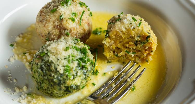 Assiette avec trois boulettes de pain savoureux dans une sauce au beurre, saupoudrées de fromage et d'herbes.