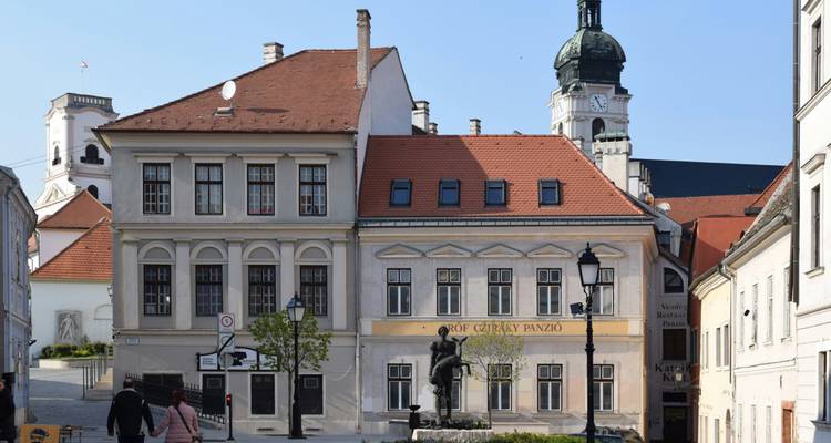 Historic square in Győr with pastel buildings and a central statue under bright daylight.
