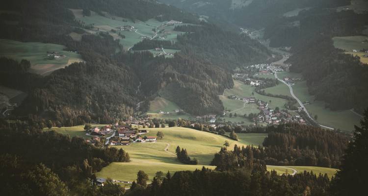 Elevated view of rolling alpine valleys with small villages and winding roads at dusk.