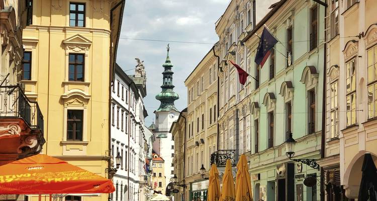 Narrow medieval street in Bratislava with colourful facades and St. Michael's Gate tower in the distance.