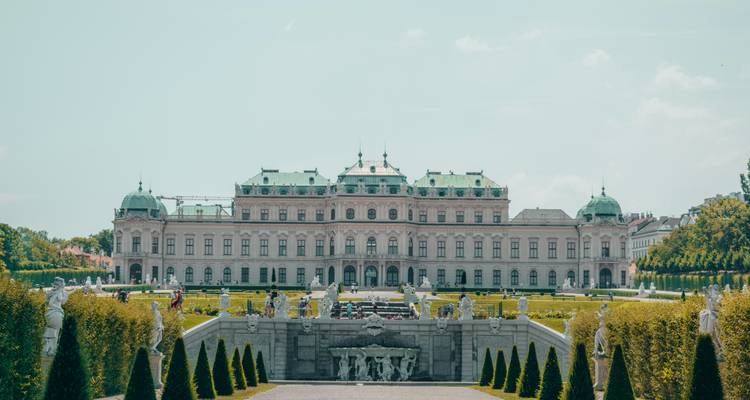 Symmetrische frontale opname van Wenen's Oberes Belvedere met verzorgde tuinen en standbeelden.