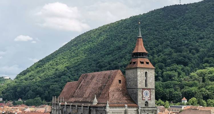 De Zwarte Kerk van Brasov tegen de achtergrond van een bebost berglandschap en pannendaken.