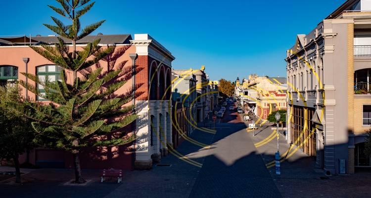 Vista de una tranquila calle de Fremantle con fachadas de edificios coloridos y una obra de arte callejera circular amarilla.