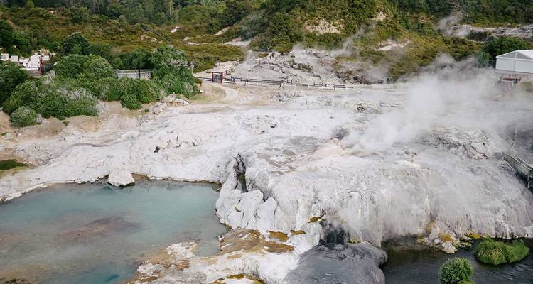 Steaming geothermal terraces and mineral pools in a volcanic area covered with sparse greenery