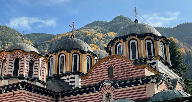 Striped domes of Rila Monastery with autumn forested mountains in background