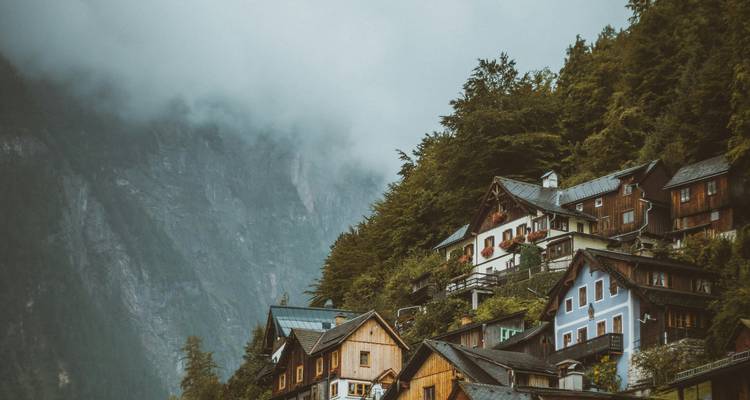 Charming alpine village houses clinging to steep hillside beneath misty cliffs
