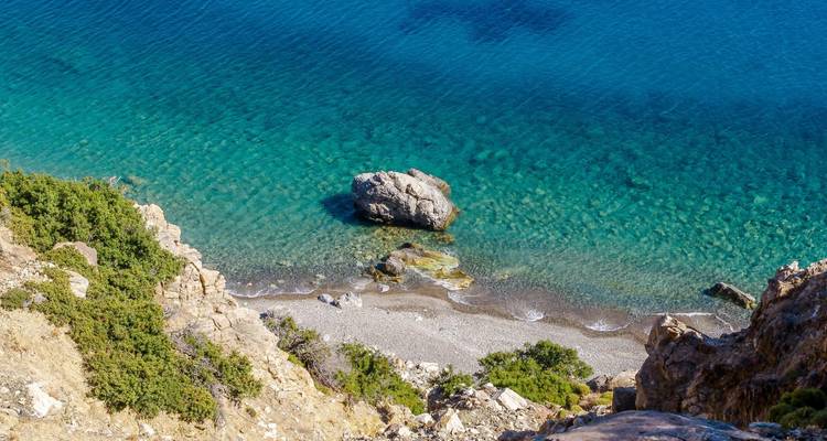Vista costera desde arriba de aguas turquesas cristalinas, una pequeña playa de guijarros y acantilados rocosos escarpados.