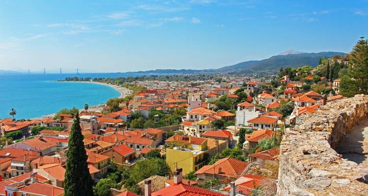 Vista expansiva sobre el pueblo costero con techos de tejas rojas, playa curva y mar turquesa bajo un cielo despejado.