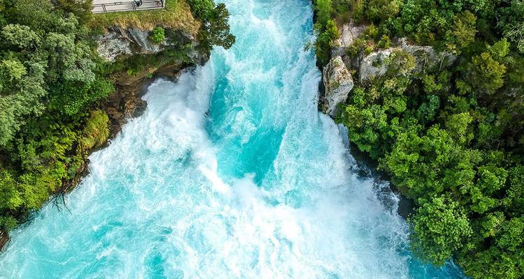 Powerful turquoise rapids plunge through a narrow rocky gorge surrounded by lush greenery.