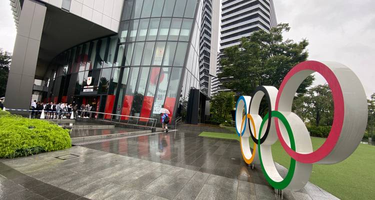 Olympic Rings monument outside modern glass building in wet weather