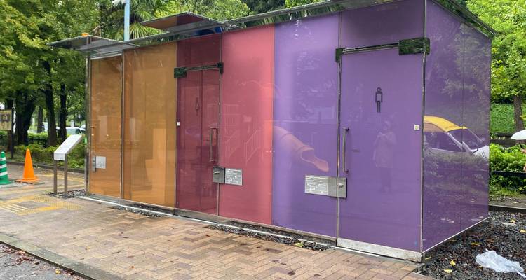 Transparent multicolored public restroom cubicles in Tokyo park on rainy day