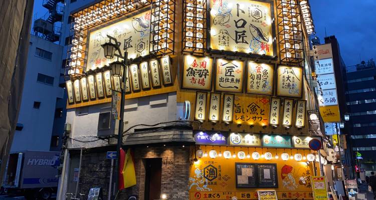 Brightly lit izakaya building with ornate lantern signs during evening blue hour