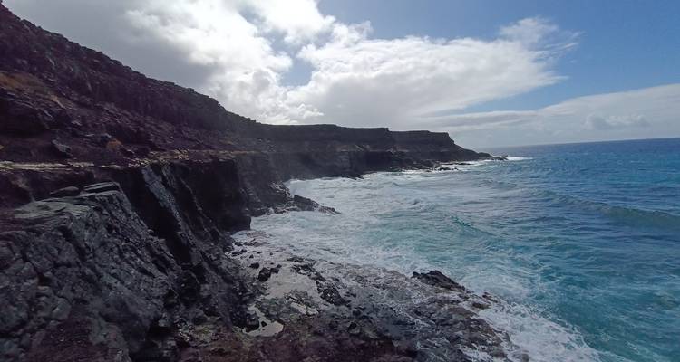 Des falaises rocheuses frappées par les vagues océaniques turbulentes sous un ciel partiellement nuageux.