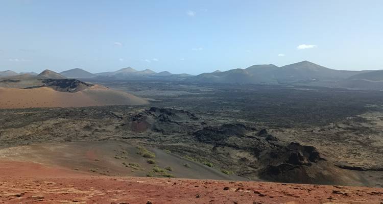 Plaine volcanique étendue avec de nombreux cônes de scories et des champs de lave rouge s'étendant jusqu'aux pics lointains.