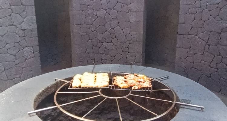Grill volcanique circulaire avec des plateaux d'aliments cuisant sur la chaleur géothermique à l'intérieur d'une structure en pierre.