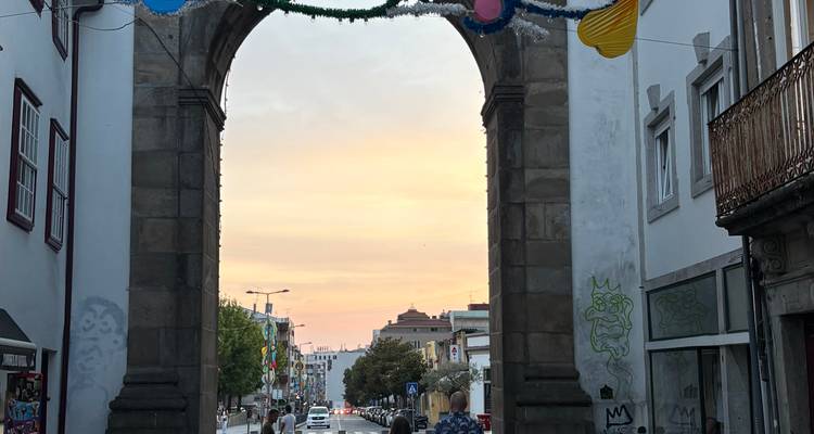Arche de pierre historique encadrant une rue de ville au coucher de soleil aux tons pastel.
