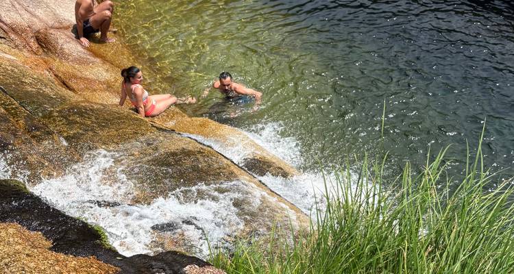 Des personnes qui nagent et se détendent à la base d'un bassin naturel alimenté par une cascade.