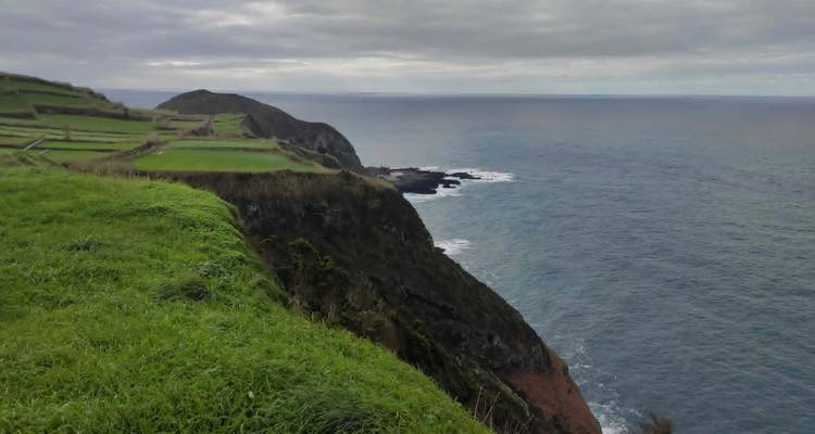 Grassy cliff tops drop steeply to Atlantic Ocean under grey skies
