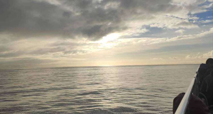 Open ocean view from a boat rail with the sun breaking through dramatic clouds.