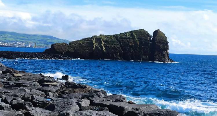 Dramatic rocky islet rising from vivid blue Atlantic waters with a distant coastline.